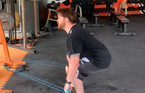 Man at the bottom of a resistance band hip hinge for glute strength and back pain